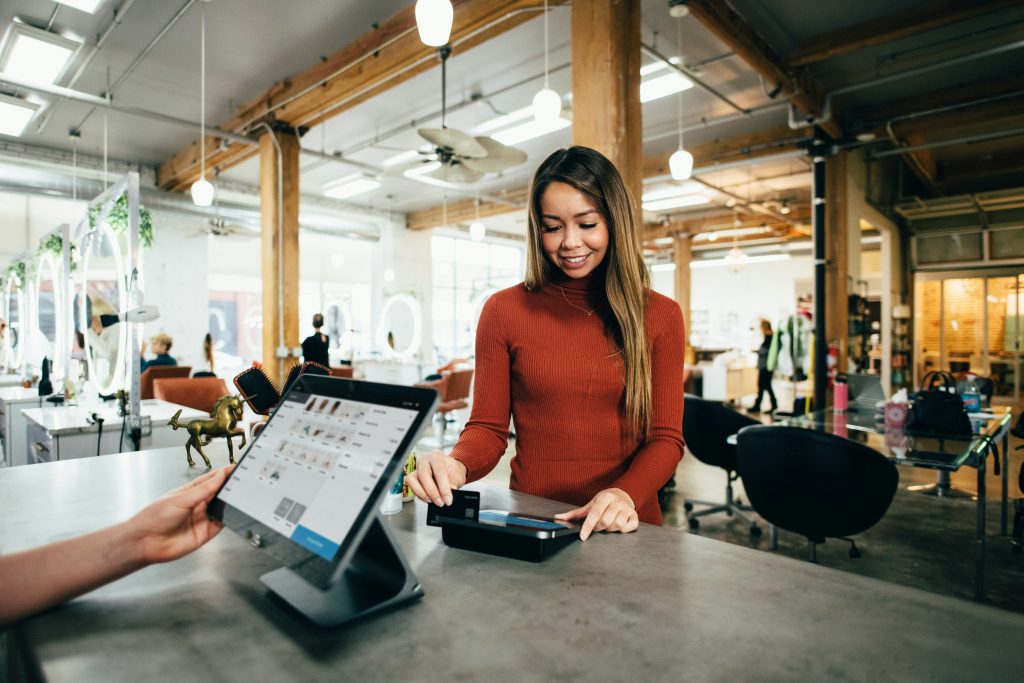 How to Identify your Customer Segments. Image shows a woman in a store, swiping her card at a POS.